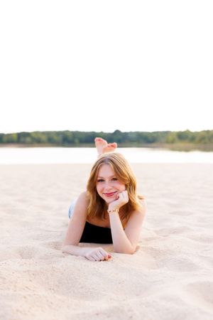 A black top is worn while relaxing on beach sand with water in background.