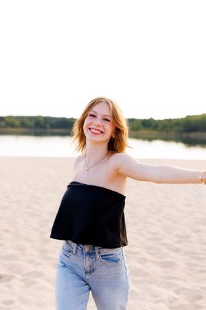 A black off-shoulder top and jeans outfit is styled on a beach at sunset.