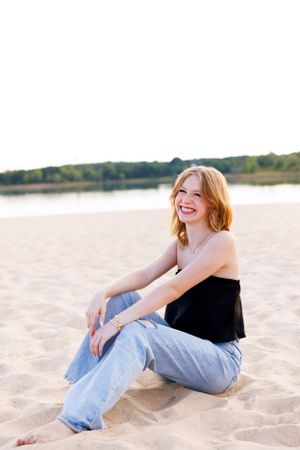 A casual black top and jeans combination is modeled on a sandy beach.