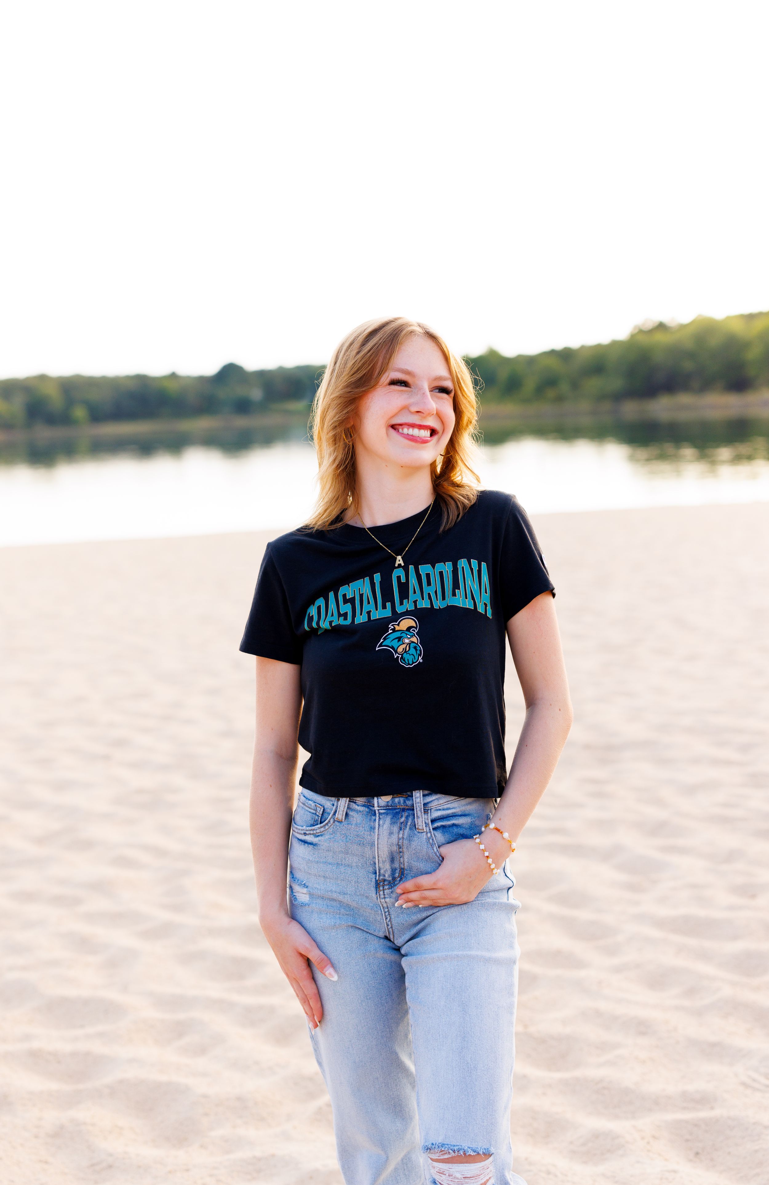 A Coastal Carolina t-shirt and light jeans are worn on a beach at sunset.