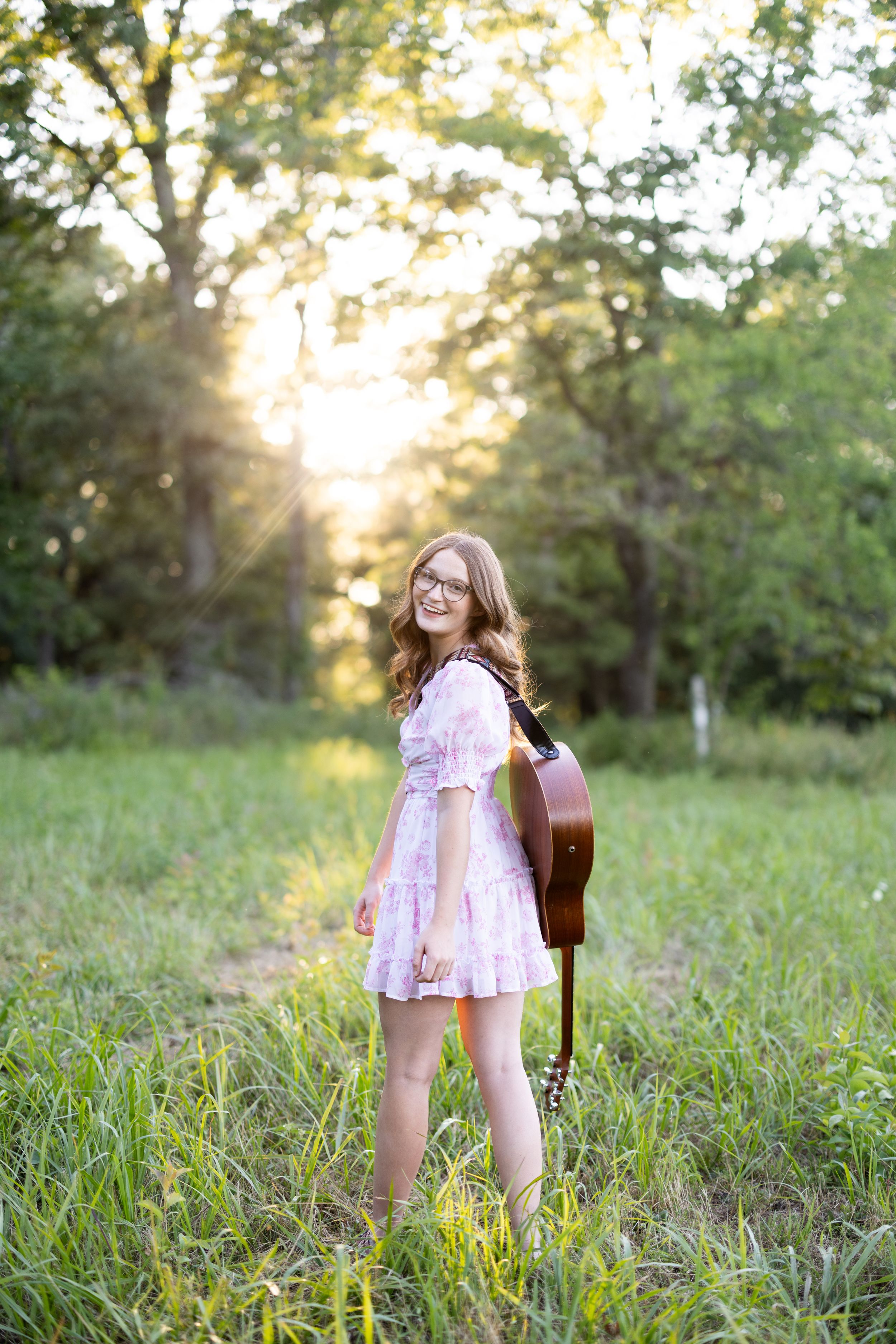 Young person in pink dress twirling in sunlit grassy field.