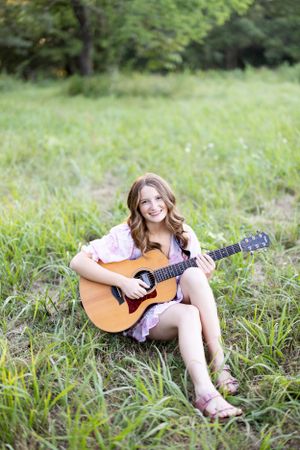 Person playing acoustic guitar while sitting in green summer meadow.