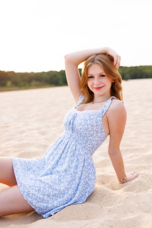 Person in blue floral sundress relaxes on sandy beach during golden hour.