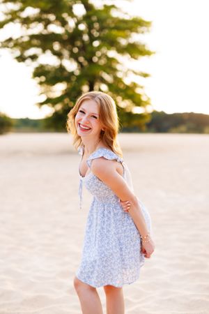 Person in light blue floral dress plays on beach at sunset.
