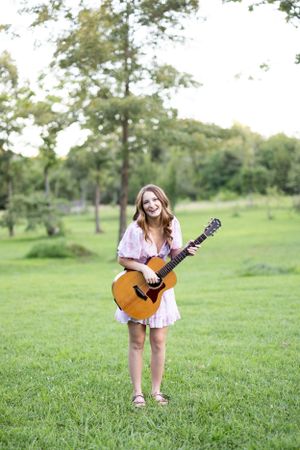 Playful poses with acoustic guitar in sunny green field.