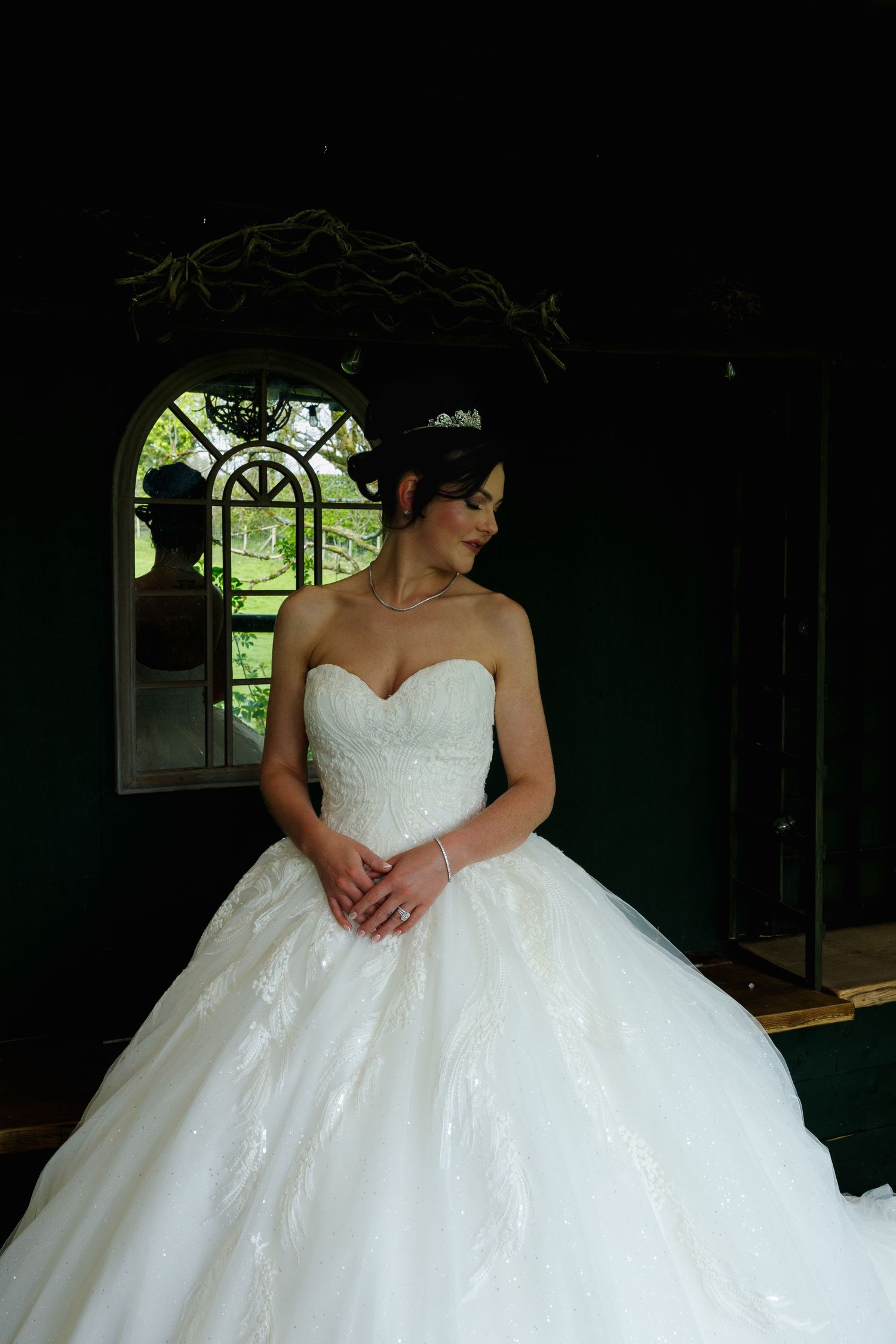 A stunning white ballgown wedding dress with sweetheart neckline photographed in a dark room with an arched window. Gibbon Bridge Hotel