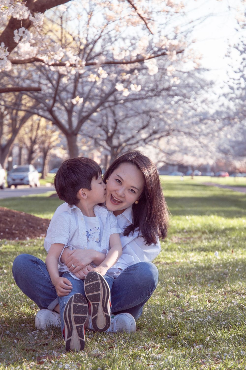 Parent and child sharing tender moment under blooming cherry blossom trees.