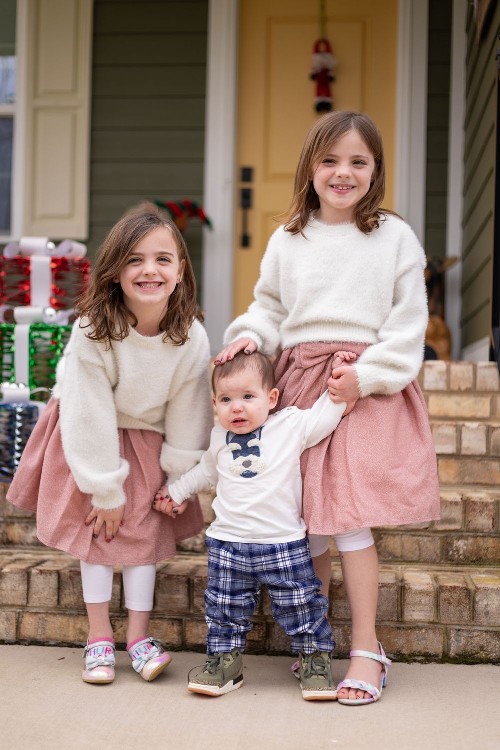 Three sequential photos show children in matching pink dresses and white sweaters sitting and playing on brick steps.