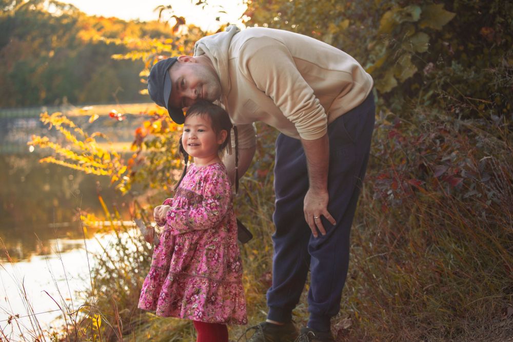 Parent and child share a peaceful moment beside a reflective lake at sunset.