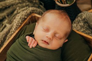 Newborn wrapped in hunter green sleeps in boho set during professional photoshoot.