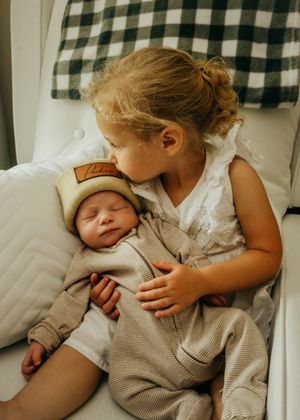 Inside golf themed nursery room big sister kisses baby brother's head while snuggling in rocker chair.