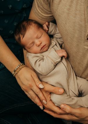 Newborn baby boy embraced by his parents during lifestyle portrait session in their home.