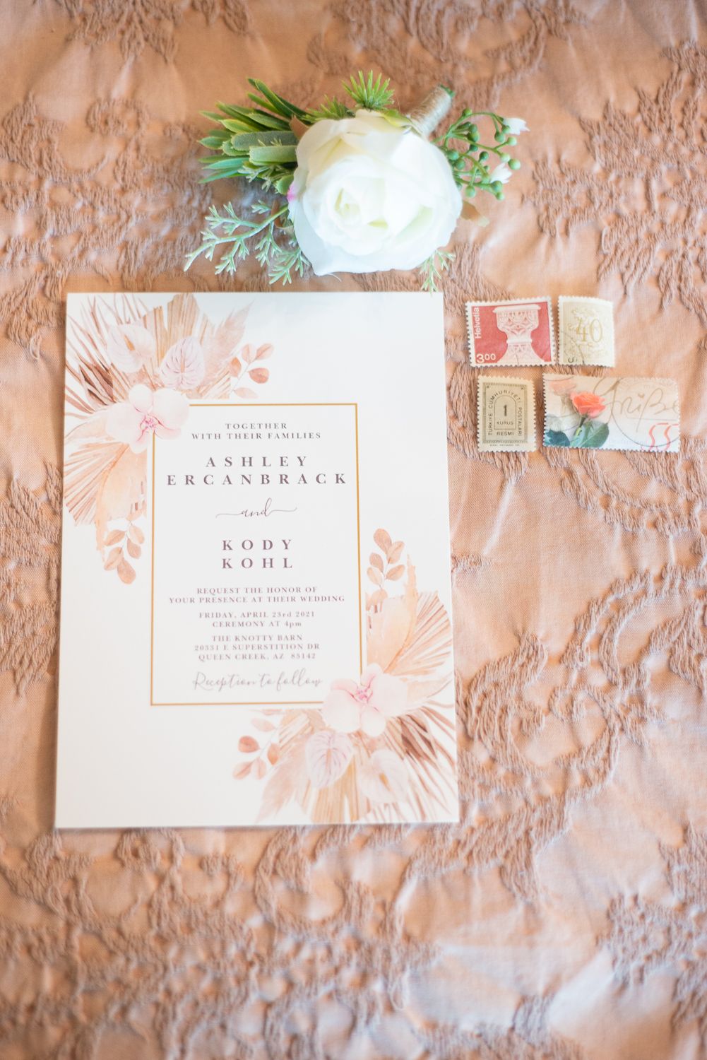 Wedding invitation with floral design and white rose on peach-colored textured background.