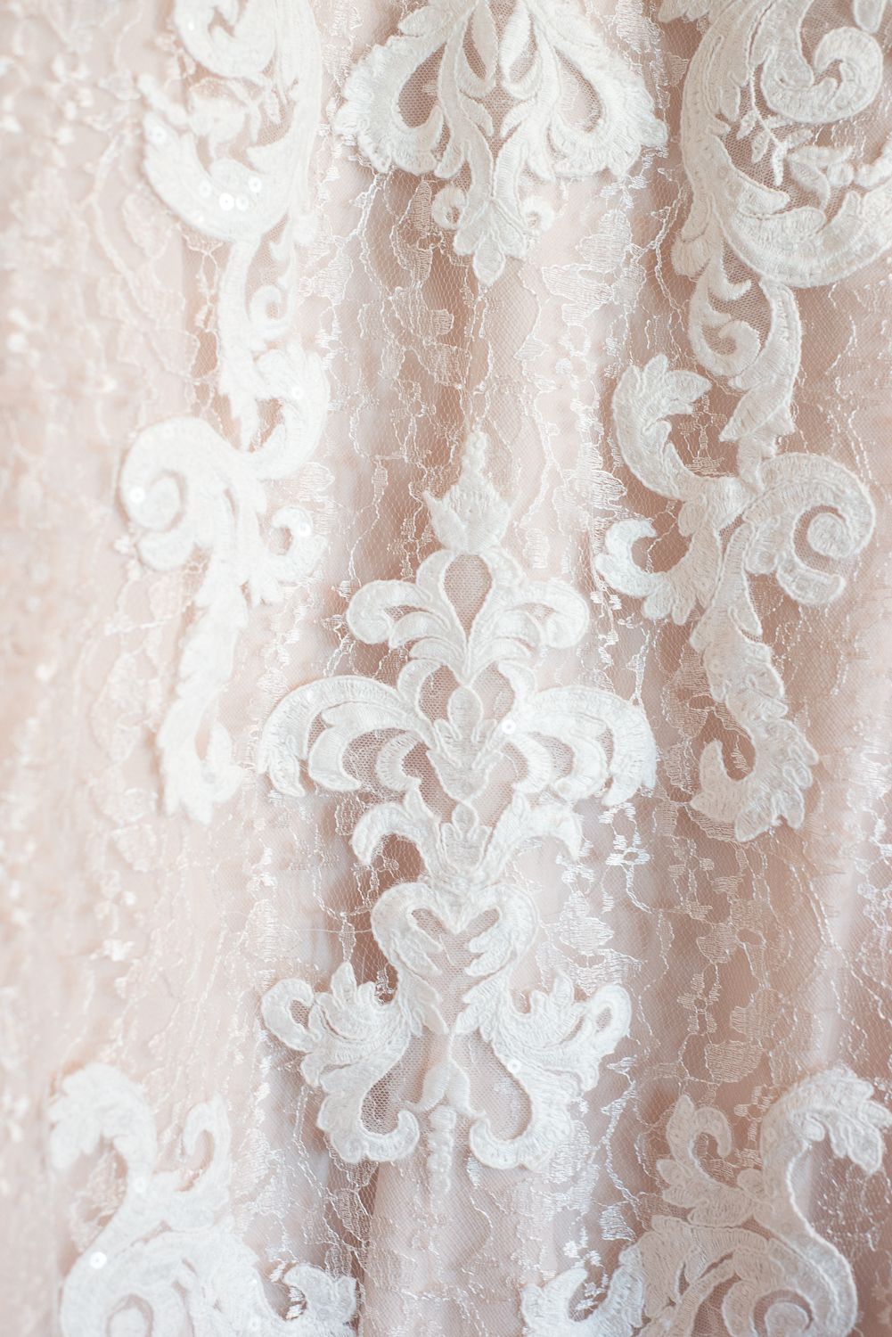 Detailed shot of blush pink lace fabric with intricate floral and damask pattern designs.