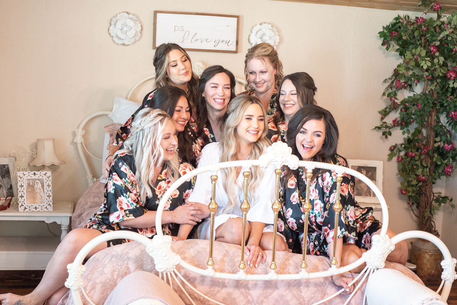 Joyful bridal party posing together on pink bedding wearing matching floral robes.