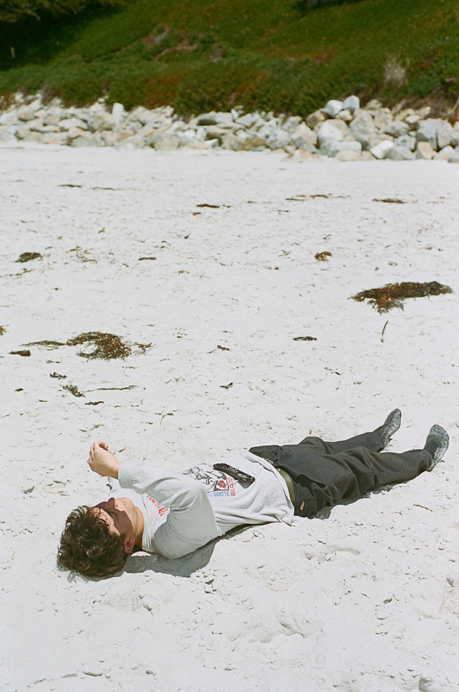 Person lying face down on white sandy beach near the ocean.