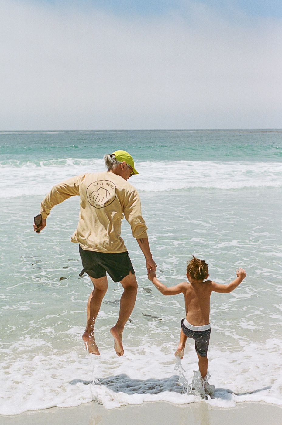 Adults and child jumping together into gentle ocean waves on a sunny beach day.