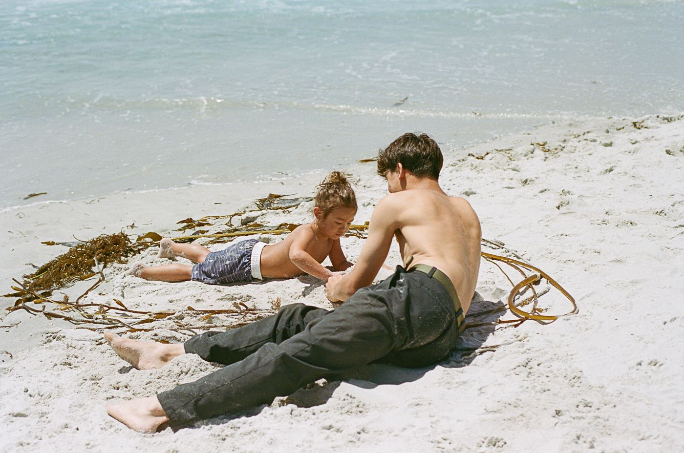 People relaxing and laying on the beach sand near ocean waves.