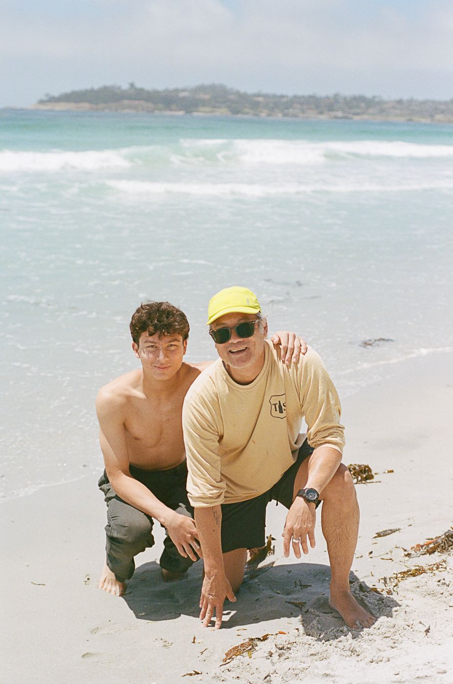 Two people crouching on wet sand at the beach with waves behind them.