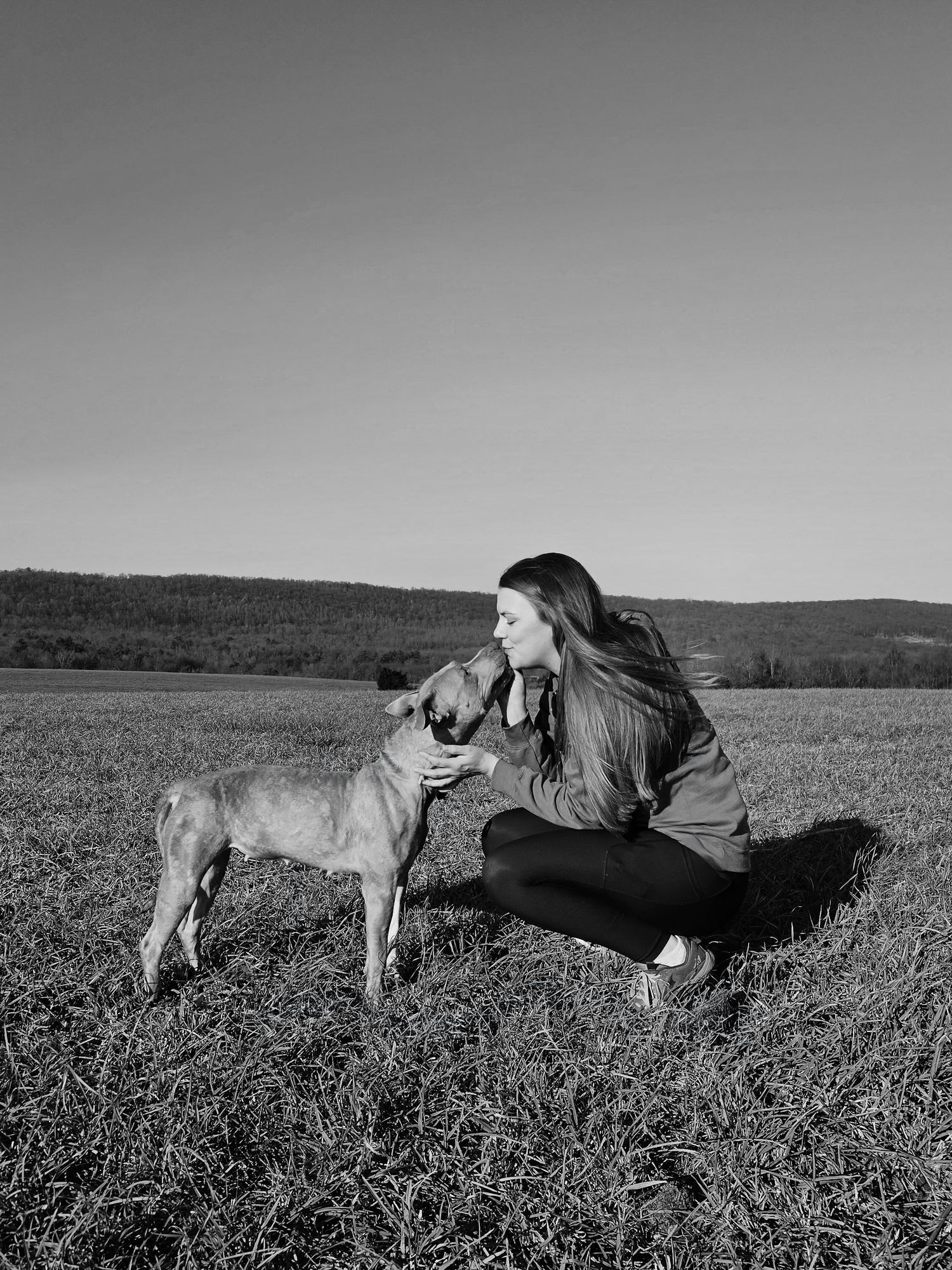 A young woman with long hair is facing a tan dog