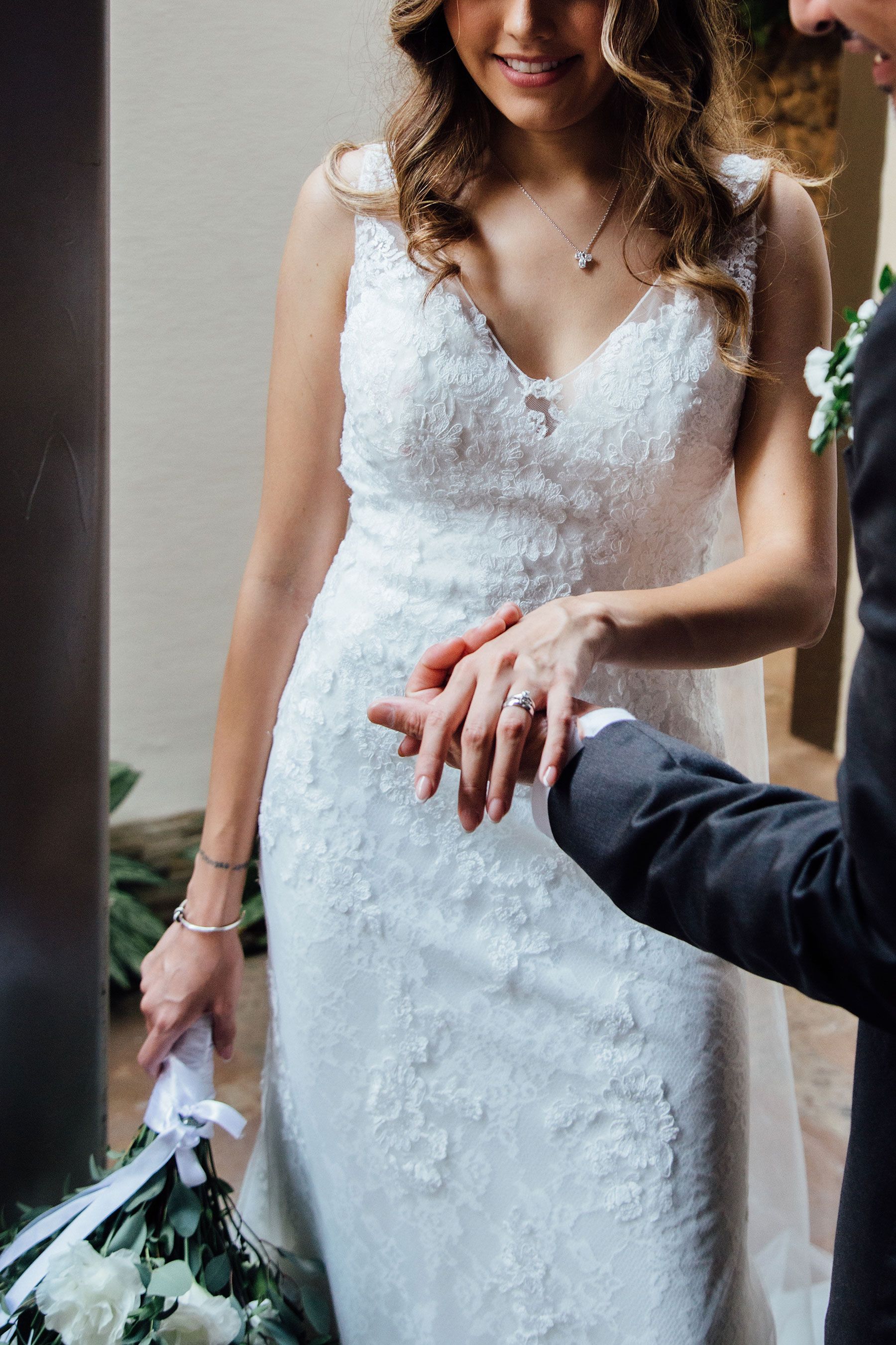 Groom places wedding ring on brides hand as she smiles in elegant white lace dress.