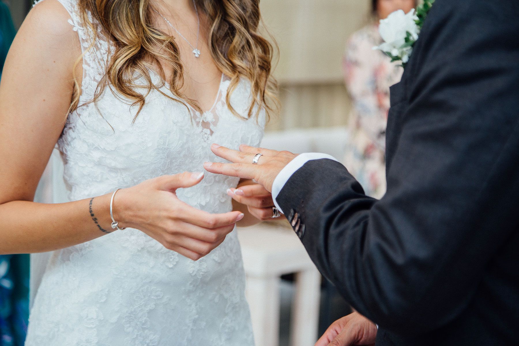 Bride placing wedding ring on grooms finger during intimate ceremony exchange.