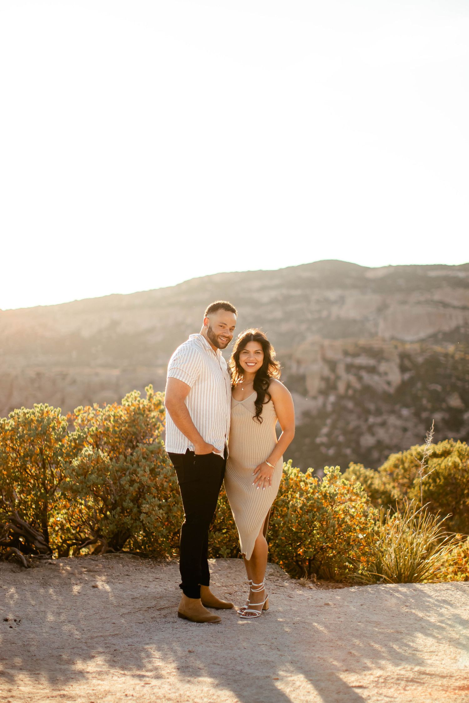 A romantic sunset engagement photo session in a mountainous desert landscape with golden lighting.