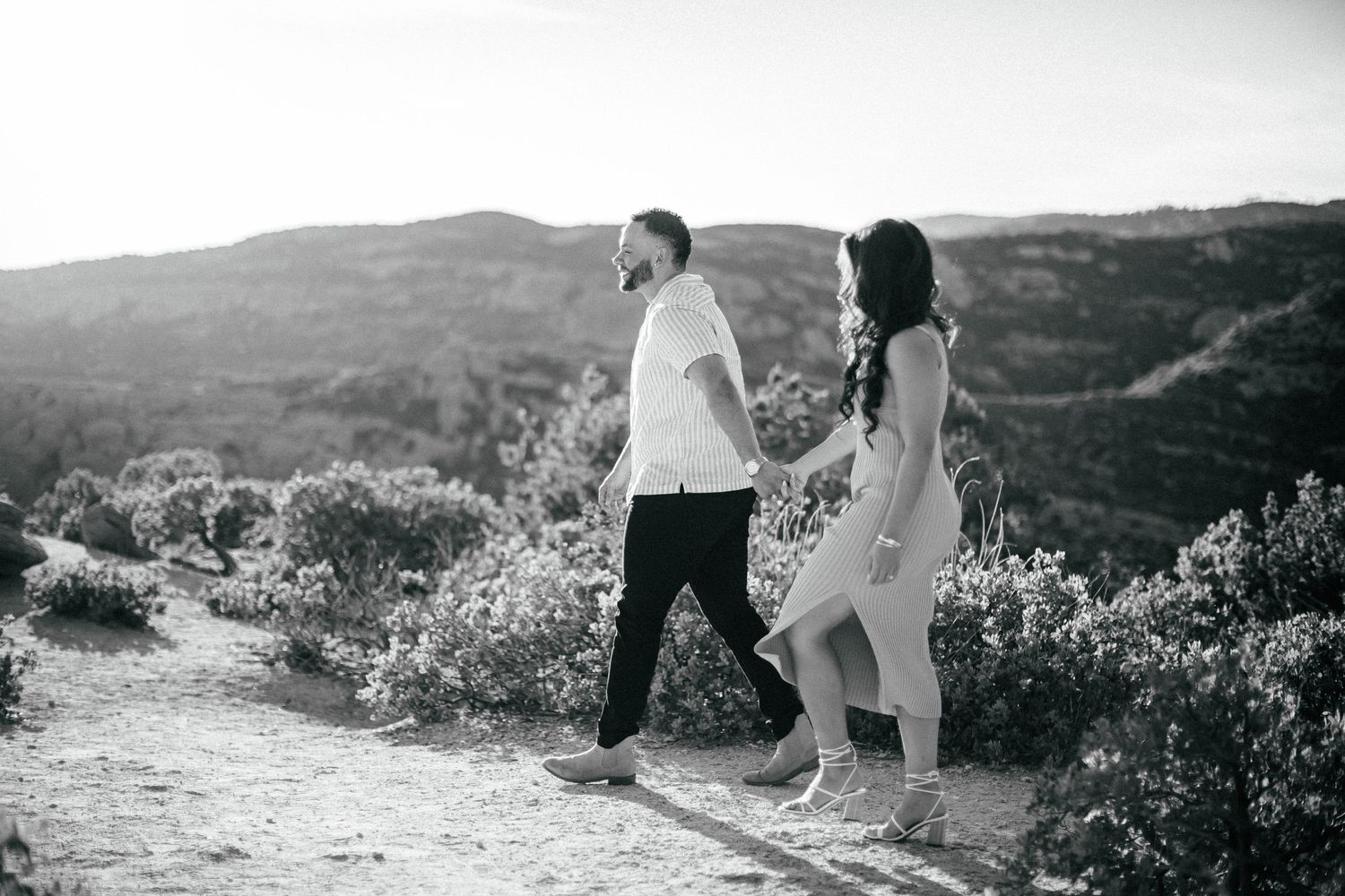 Black and white photo of a couple walking together on a mountain path during sunset.