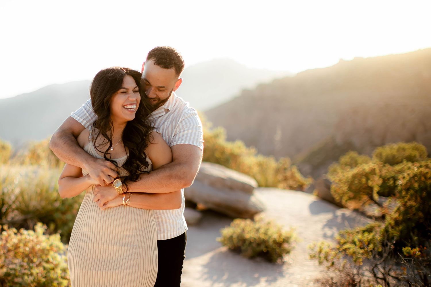 Couple embracing during golden hour with desert mountains and wildflowers in the background.
