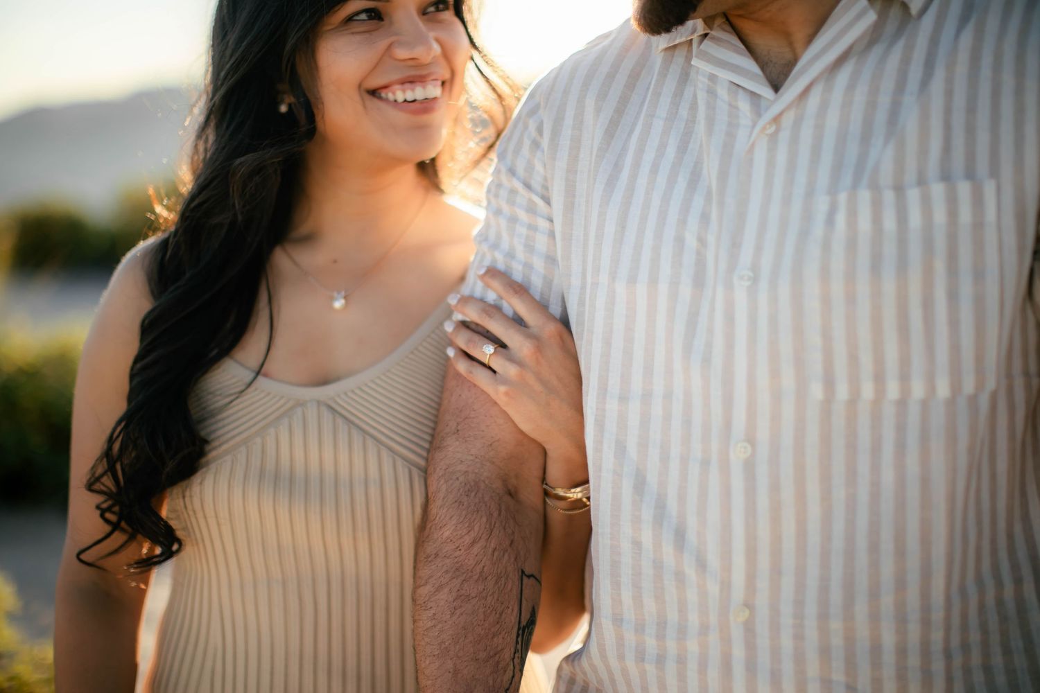 Intimate portrait of a couple in casual attire against a mountain backdrop during sunset.