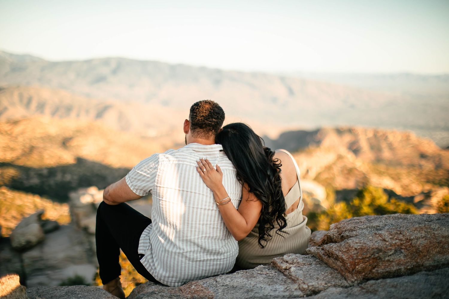 Couple sitting together on rocky overlook with scenic desert mountain vista in background.