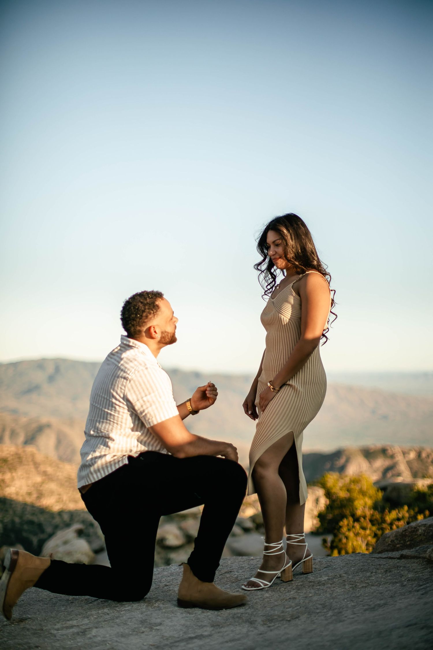 A proposal moment captured on a mountain overlook with desert landscape in background.