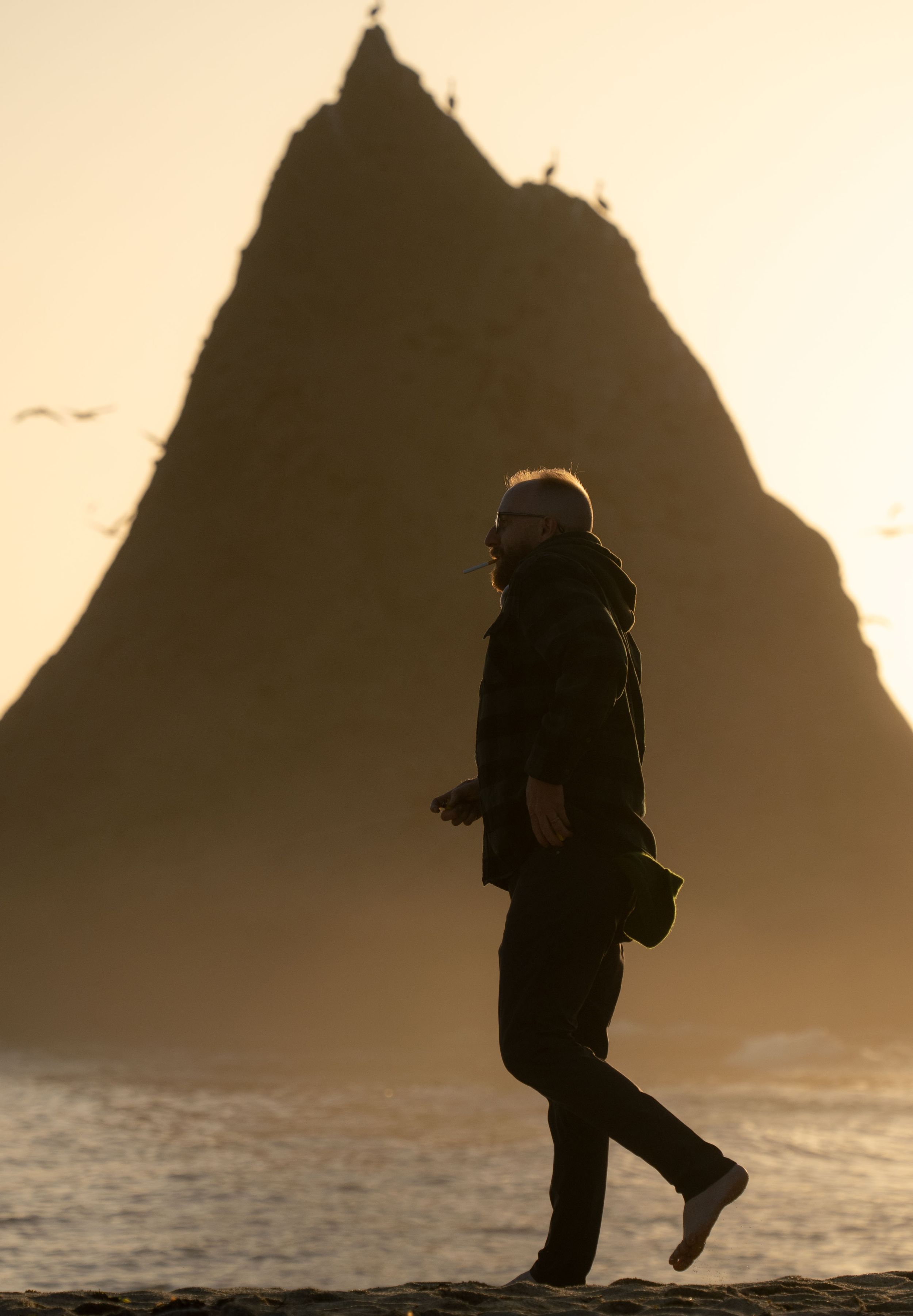 A dark silhouette of a person walking along a cliff edge at sunset.