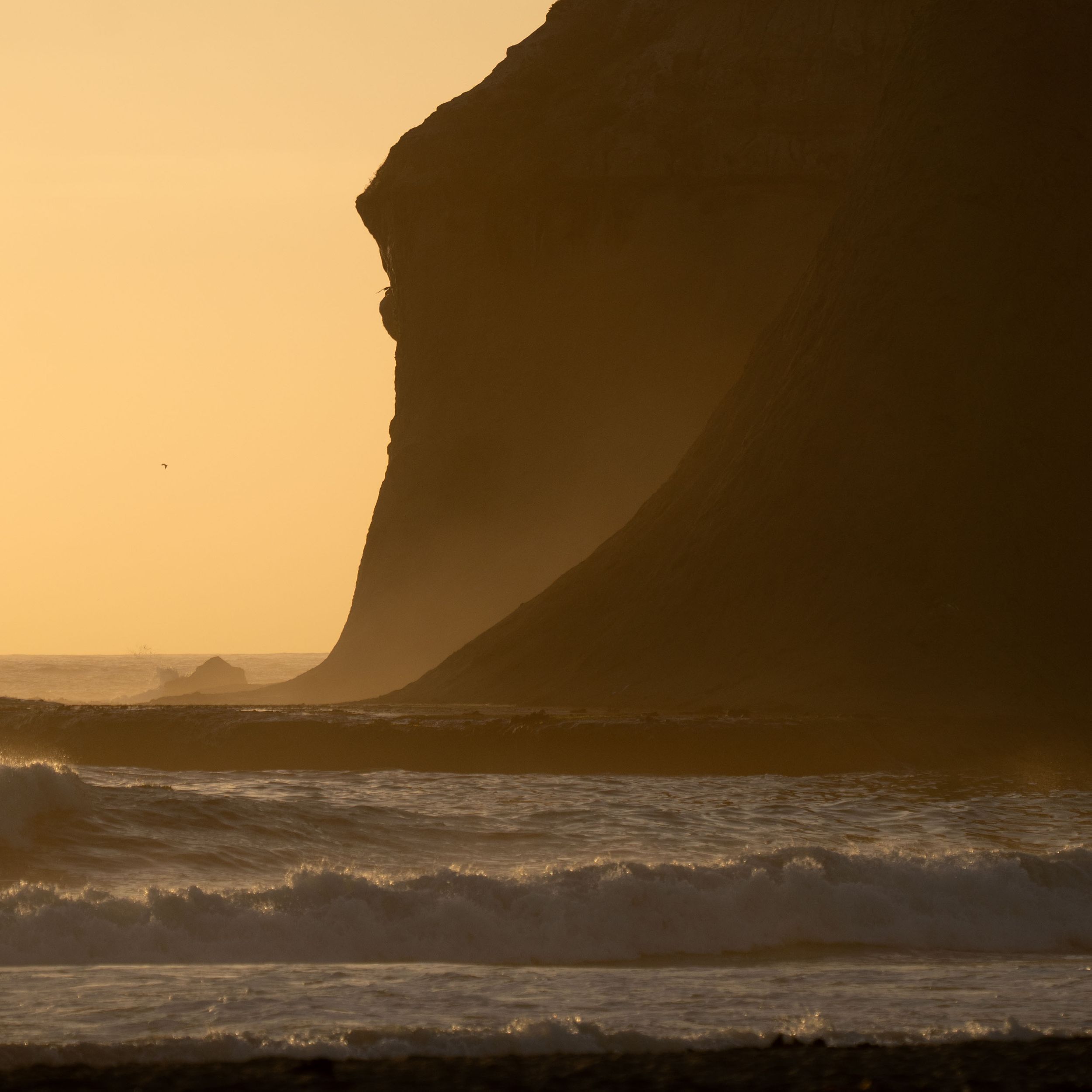 Ocean waves crash against rocky cliffs during golden hour.