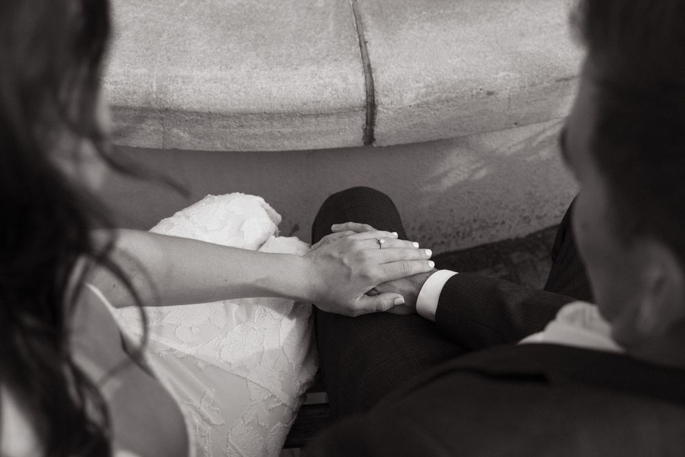A black and white detail shot of hands clasped together near a fountain edge.