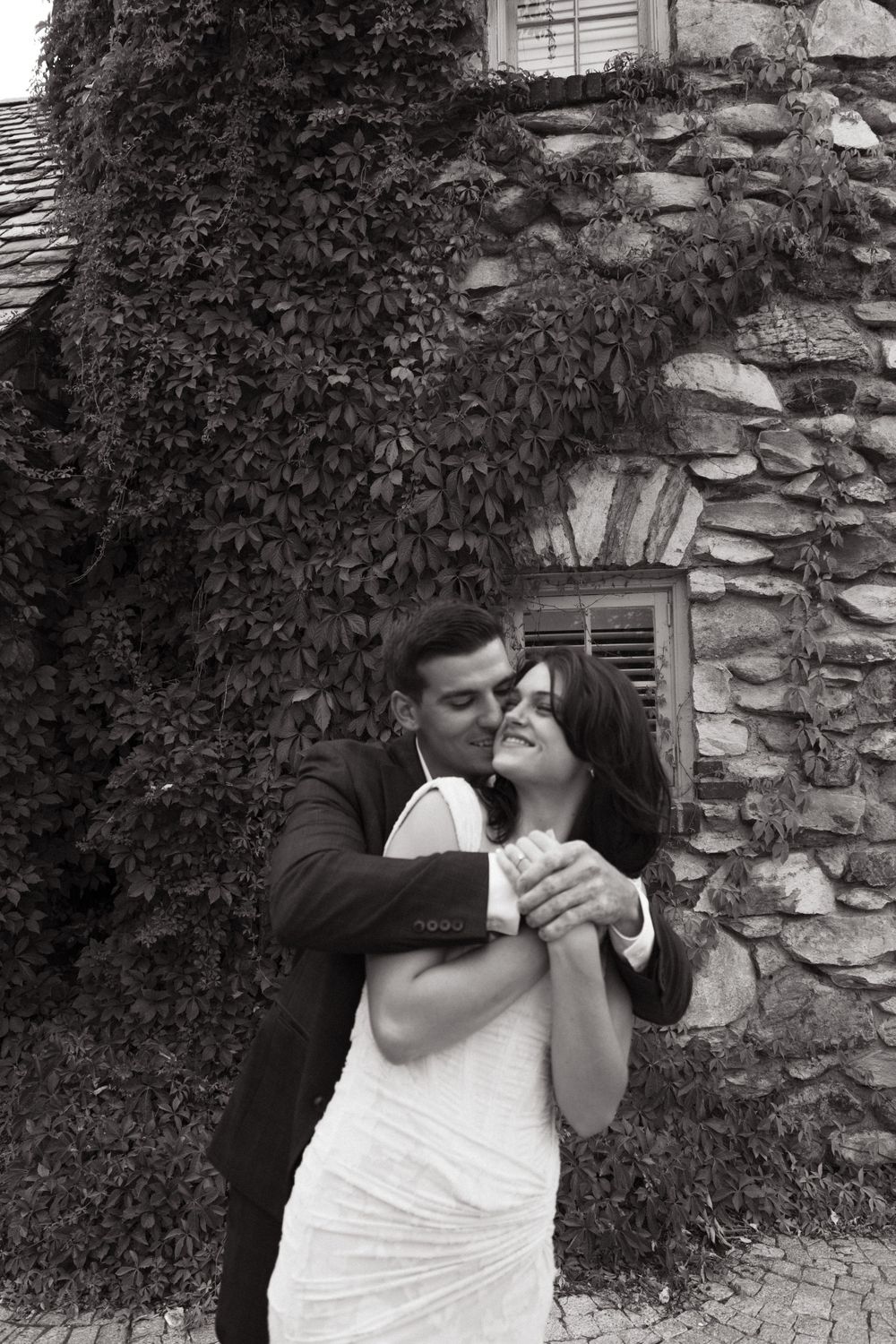 A tender black and white moment captured against a vine-covered stone wall.