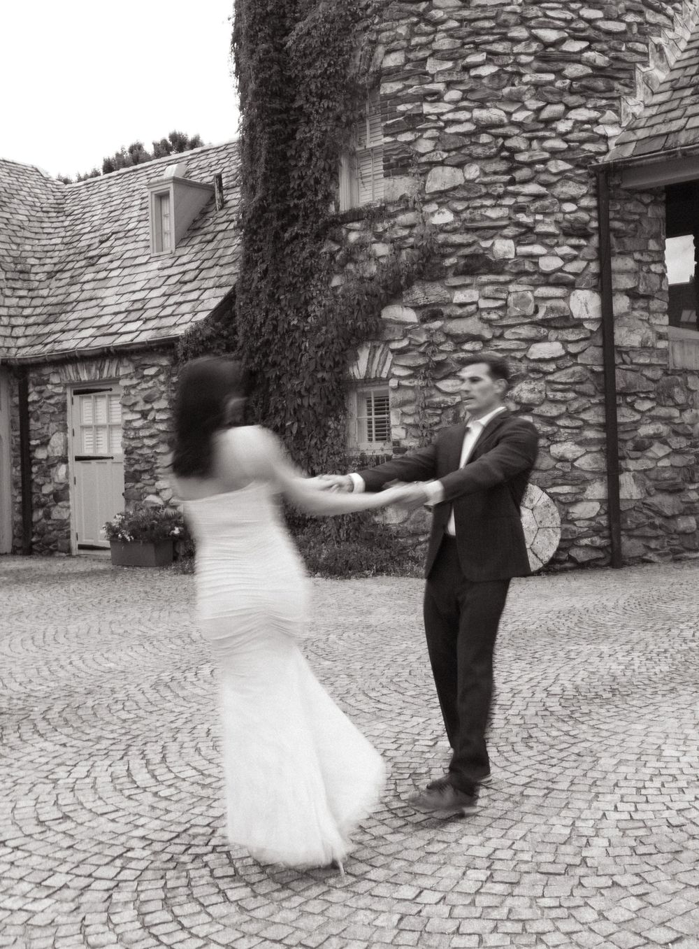 A black and white photo of a dancing couple in front of a historic stone tower.