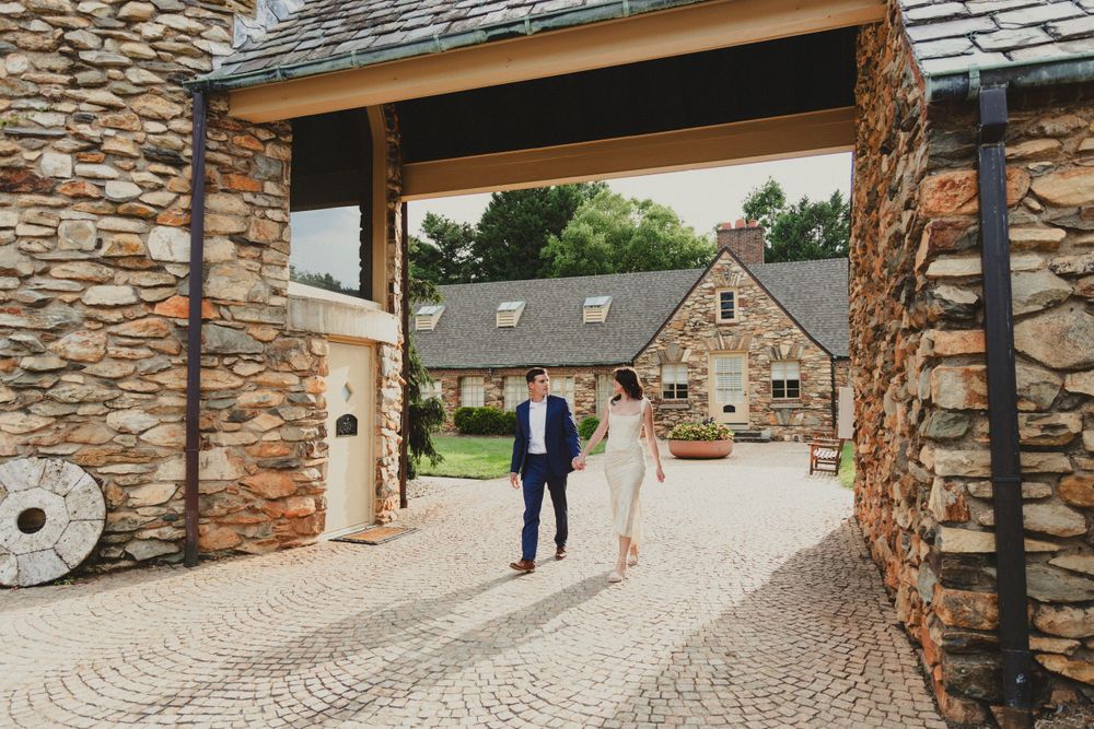 Couple walking through stone archway entrance of rustic wedding venue.