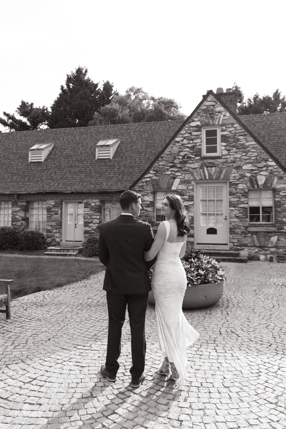 Couple standing in front of charming stone cottage with cobblestone path.