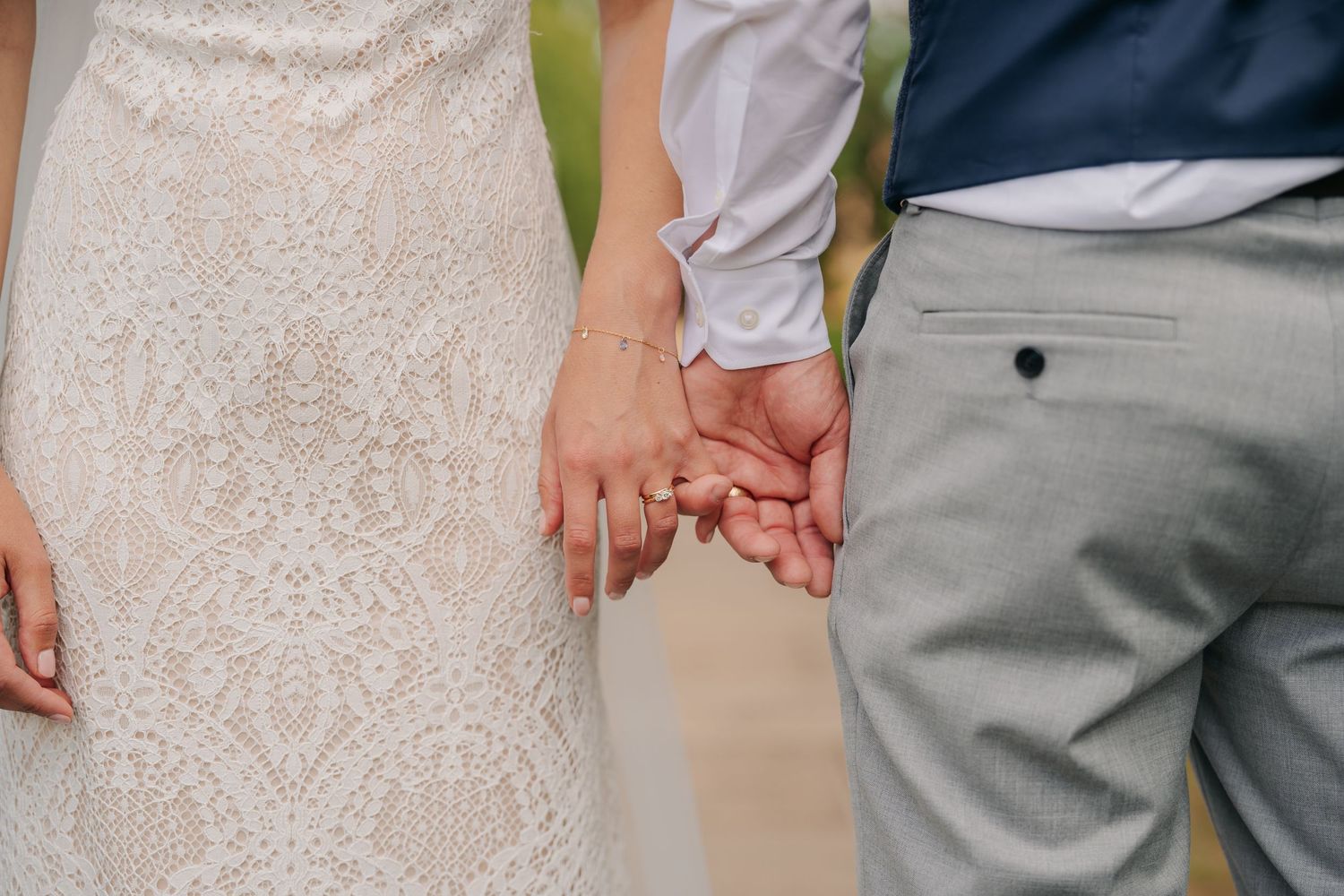 Close-up shot of hands exchanging wedding rings with colorful roses and eucalyptus bouquet in the foreground.