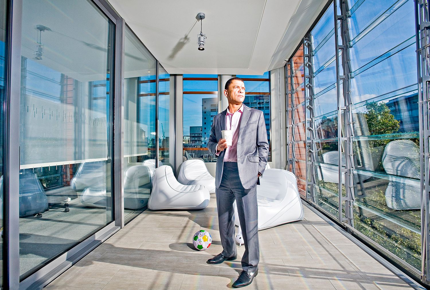 A professional stands in a modern office space with glass walls and white lounge furniture.