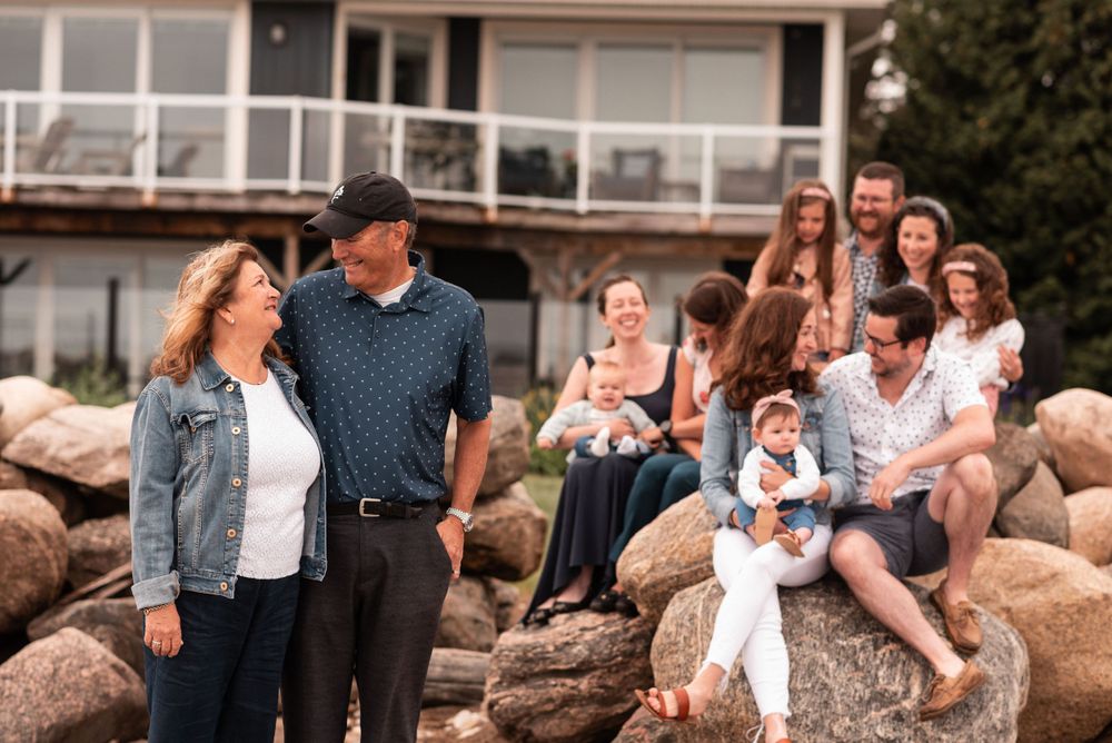 Multi-generational family posed on rocky shoreline with house in background.