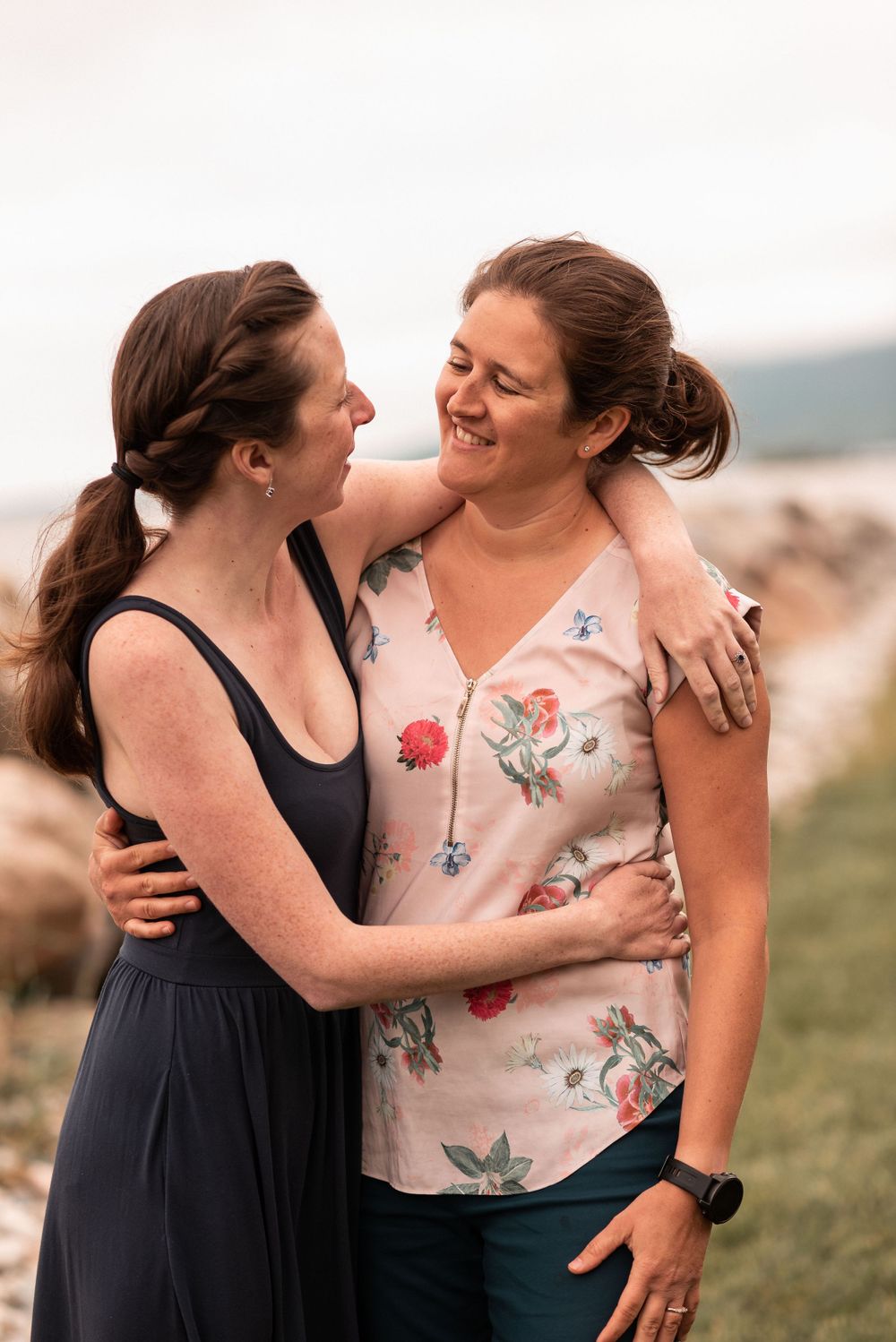 Two people embracing and laughing together on grassy hill by the ocean.