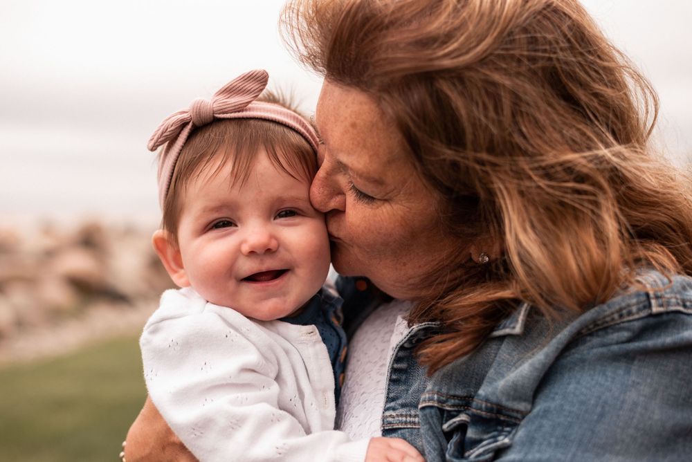 Tender moment of affection between parent and smiling baby with pink bow outdoors.