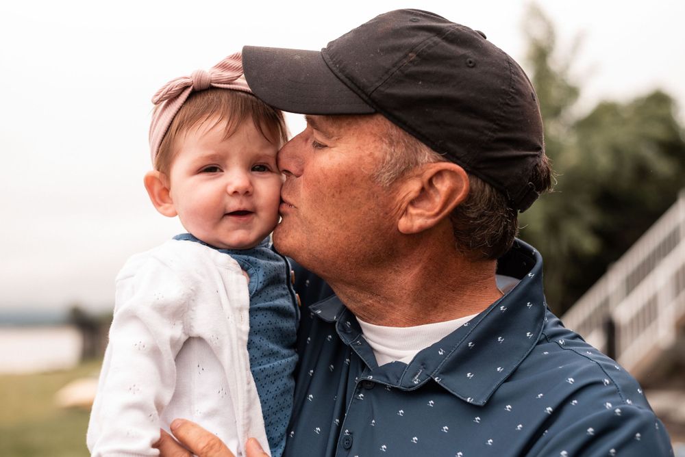 Intimate close-up of parent giving baby in white outfit a kiss outdoors.