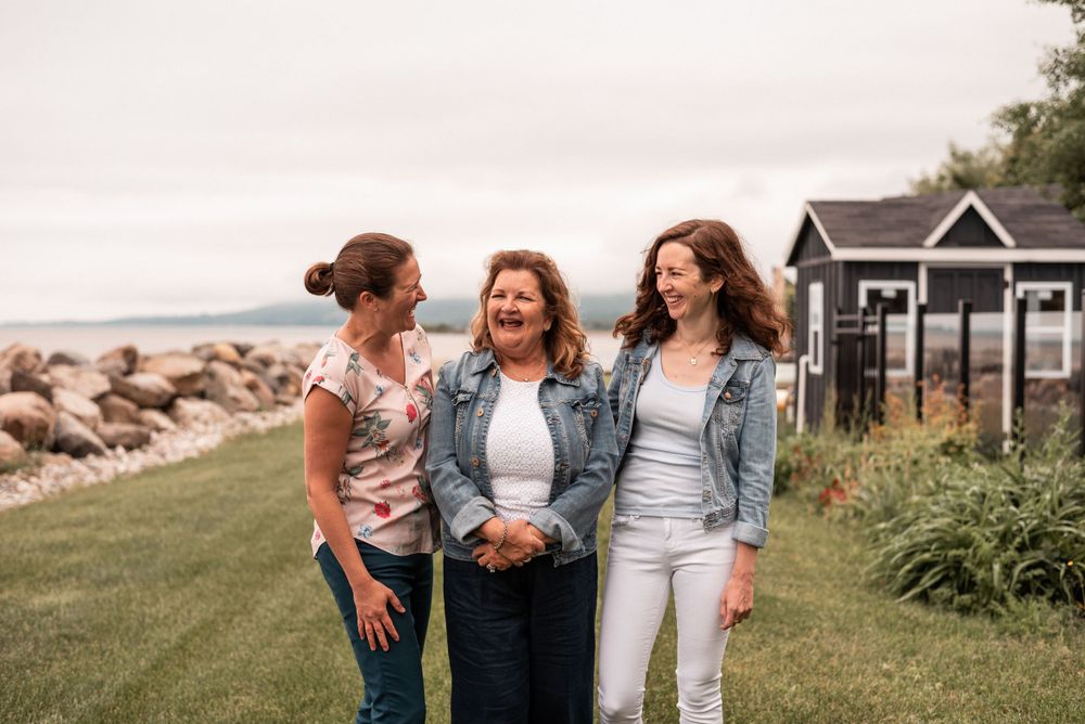 Three people laughing together outdoors with coastal scenery in background.