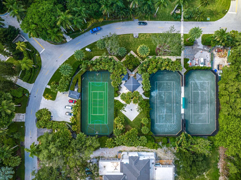 Bird's eye view of three tennis courts surrounded by tropical landscaping and curved pathways.