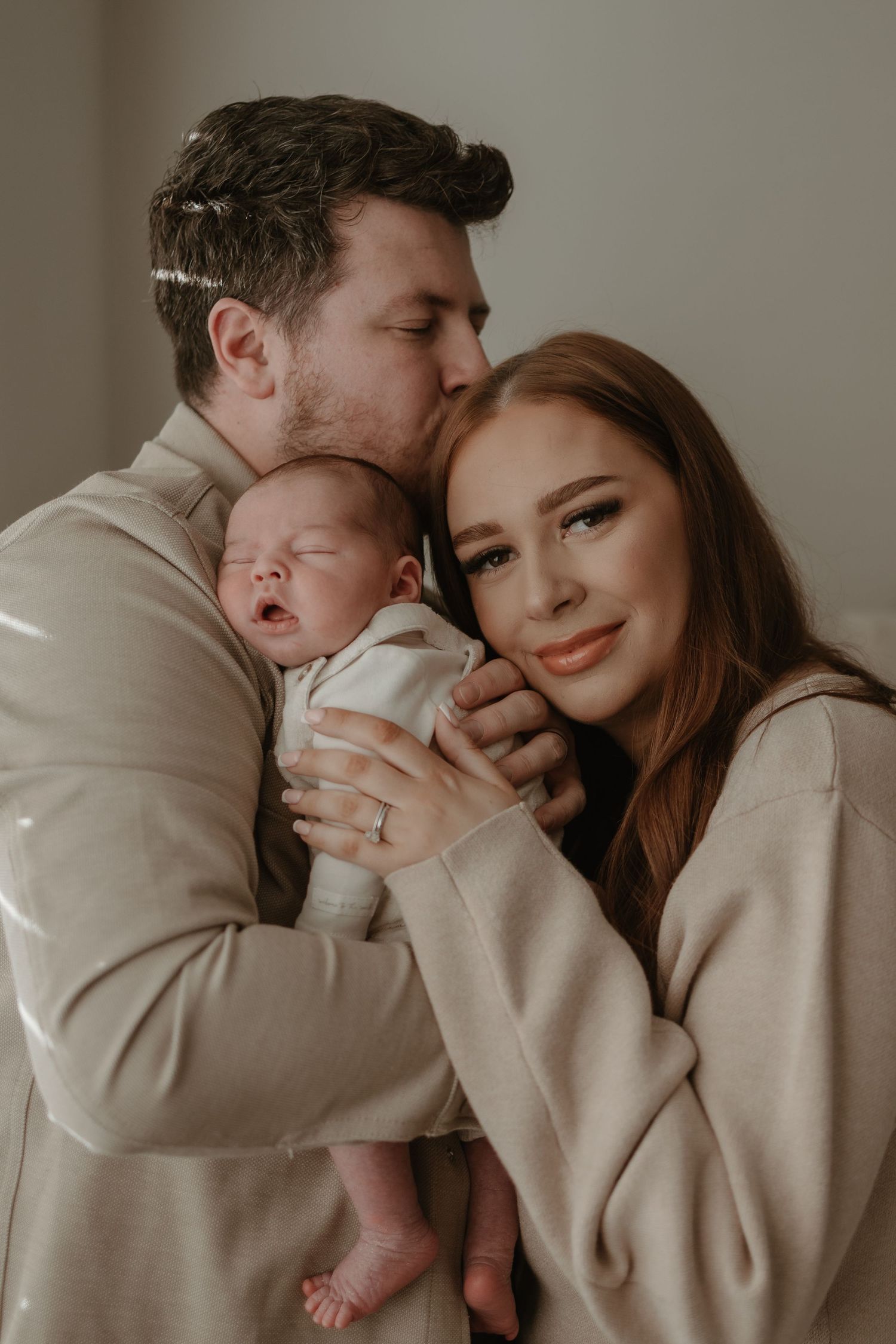 Intimate family portrait showing tender moments between parents and newborn in neutral tones.