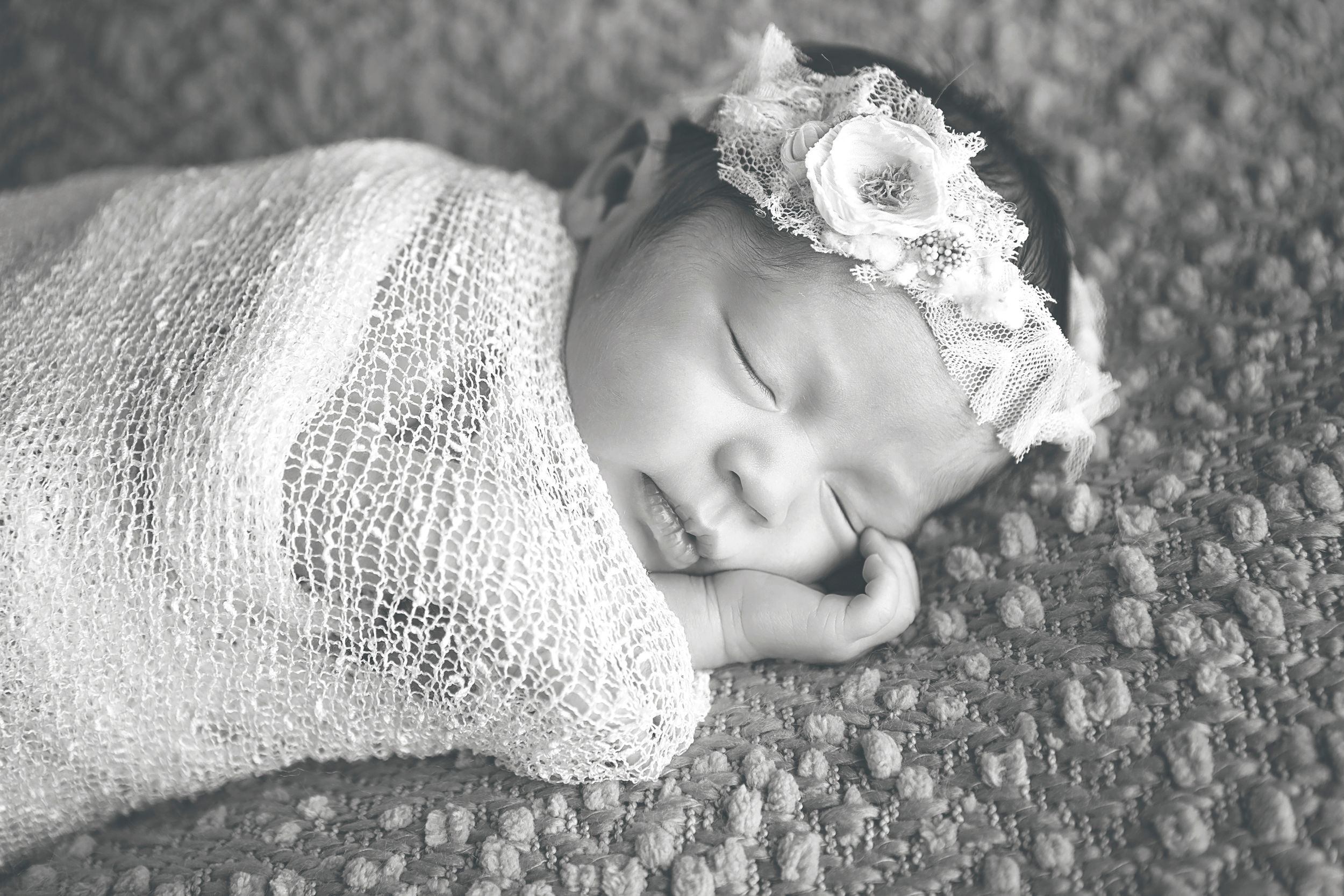 Newborn baby sleeping peacefully in white wrap on textured surface.