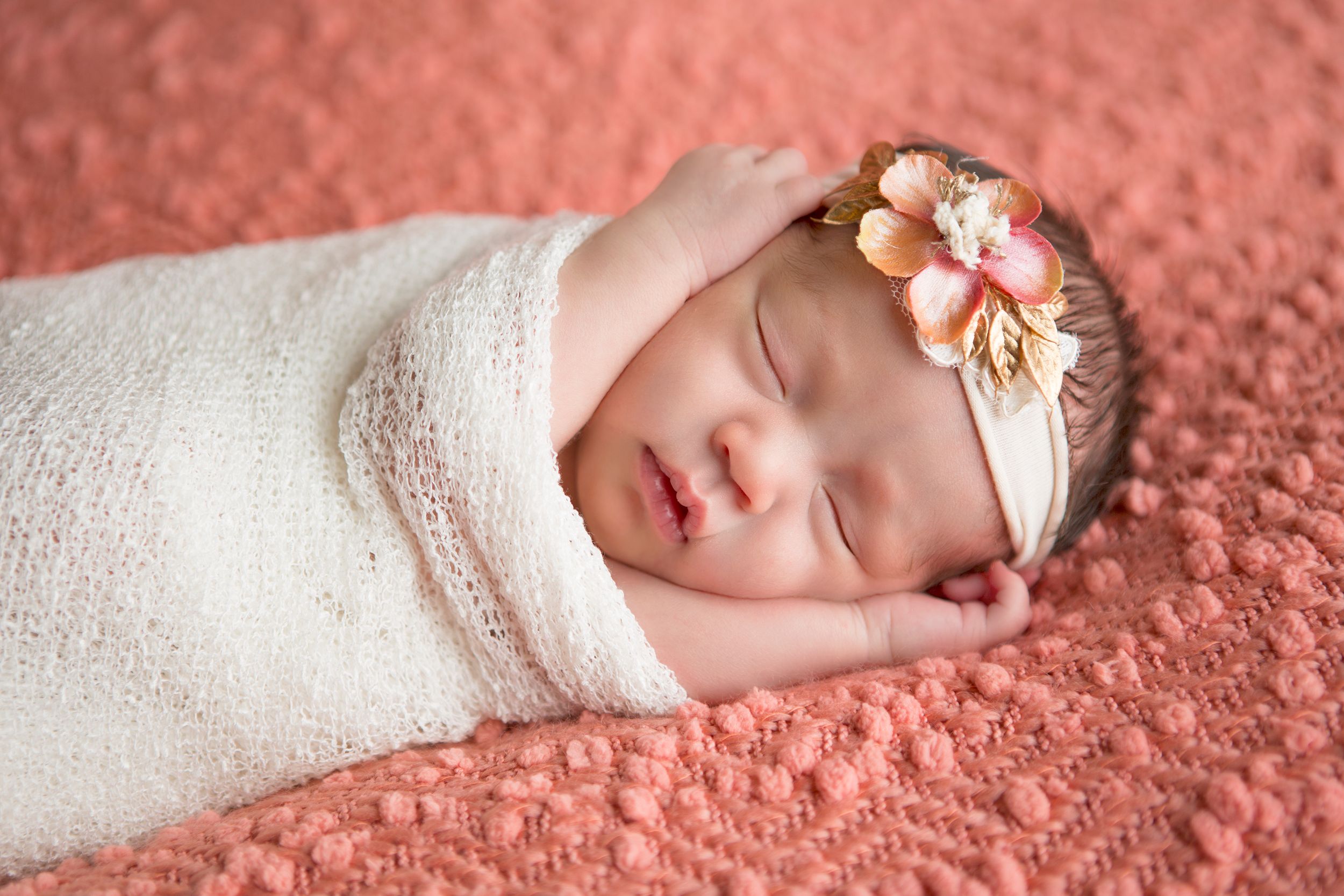 Sleeping newborn wrapped in white blanket on pink textured background.